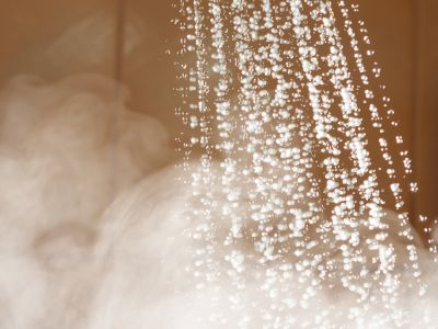 Water droplets cascading from a showerhead, illustrating the endless hot water supply of a tankless water heater, with steam in the background emphasizing warmth and comfort.